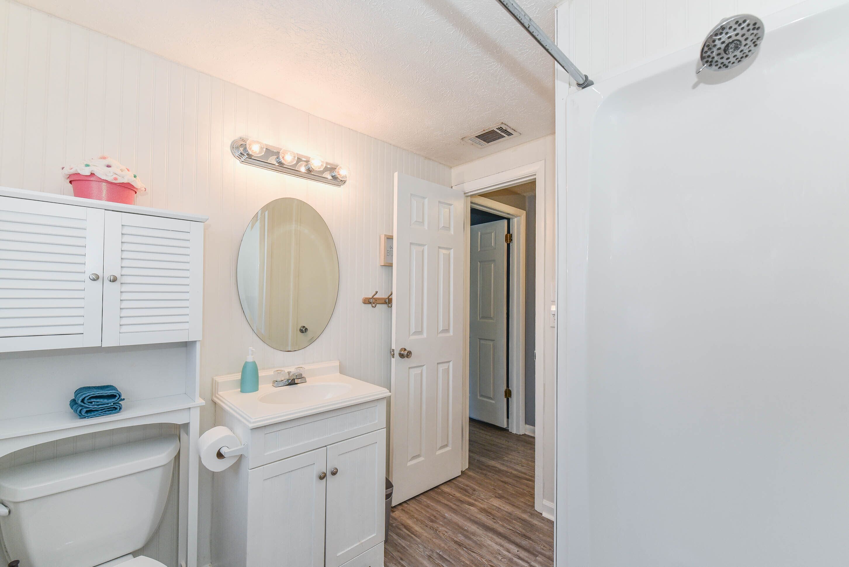 A bathroom with a toilet, sink, mirror, and a door leading to another room.
