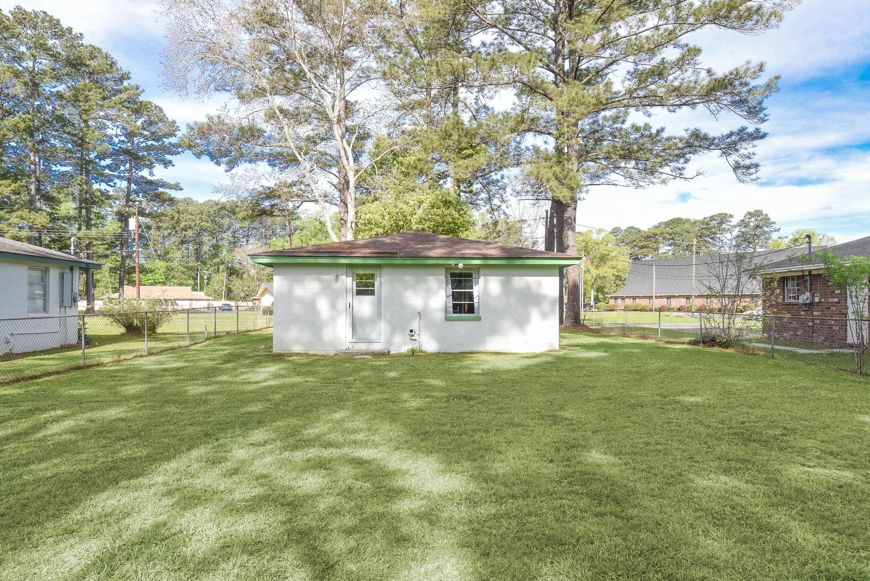 A small white house with a green trim and a red roof, surrounded by a well-maintained lawn and tall trees.