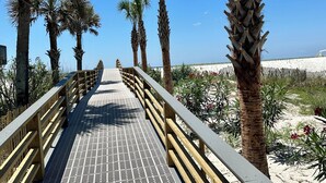 A wooden boardwalk leading to a beach with palm trees and a clear blue sky.