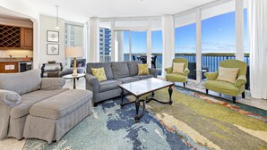 A spacious living room with a large window, a ceiling fan, and a view of the ocean.