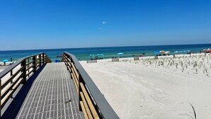 A beach with a wooden boardwalk leading to the shore, clear blue sky, and ocean view.
