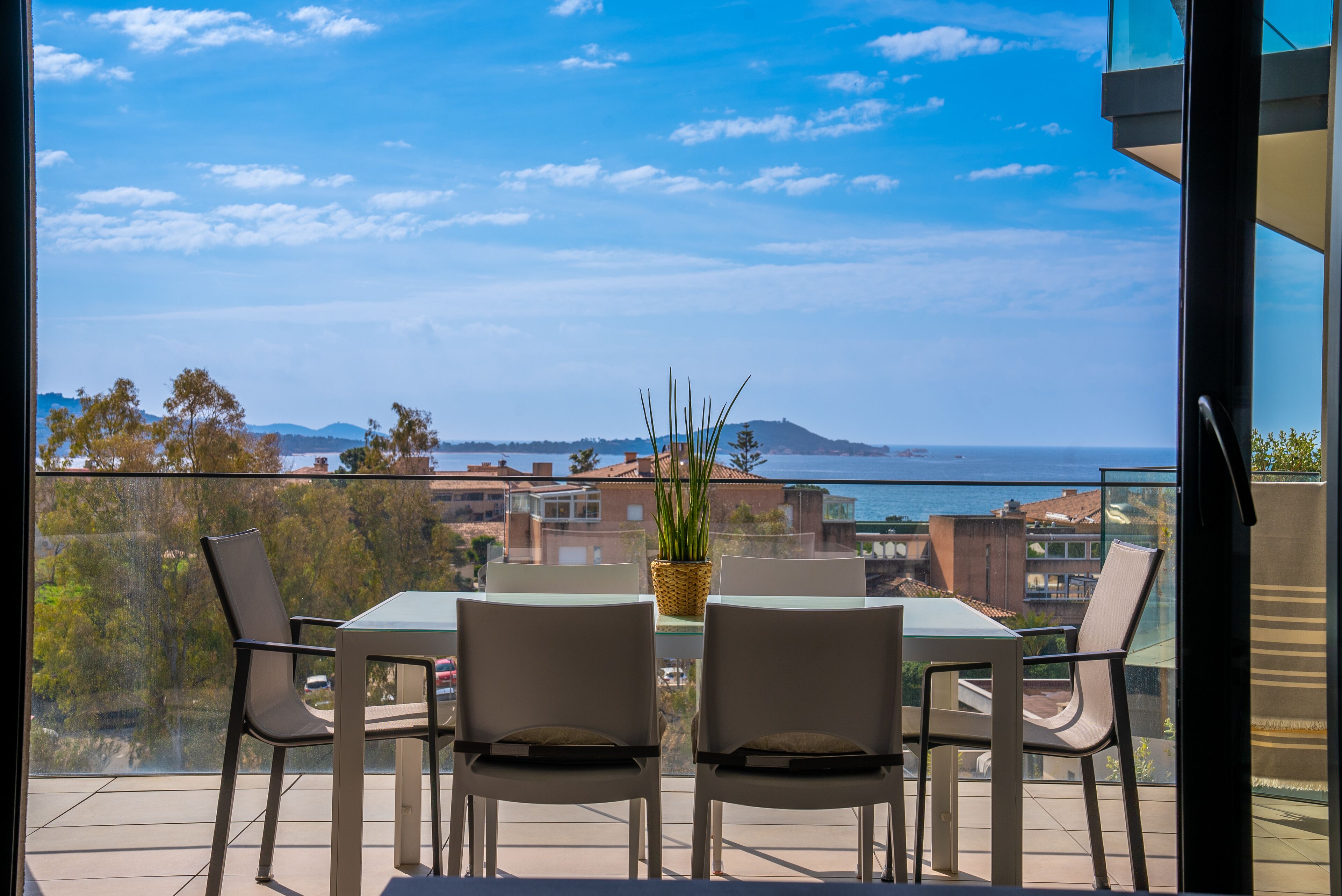 Un balcón con mesa y sillas, con vistas a la costa, edificios y una montaña a lo lejos.