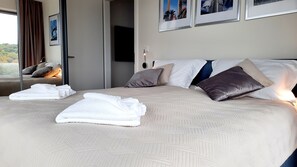 Une chambre d’hôtel dotée d’un grand lit, de plusieurs oreillers, d’un téléviseur à écran plat et d’une fenêtre donnant sur un paysage verdoyant.