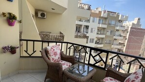 A balcony with wicker furniture, a glass table, and potted plants.