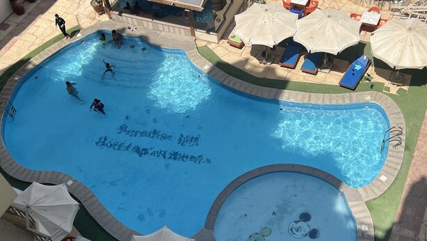 A swimming pool with a unique design, surrounded by lounge chairs and umbrellas.