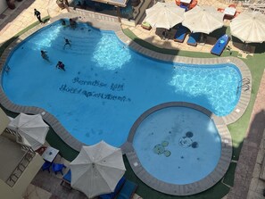 Une piscine au design original, entourée de chaises longues et de parasols.
