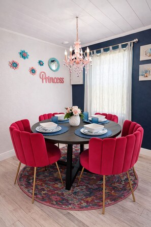 Une salle à manger avec une table ronde, des chaises rouges, un lustre et un panneau indiquant «Princesse» sur le mur.