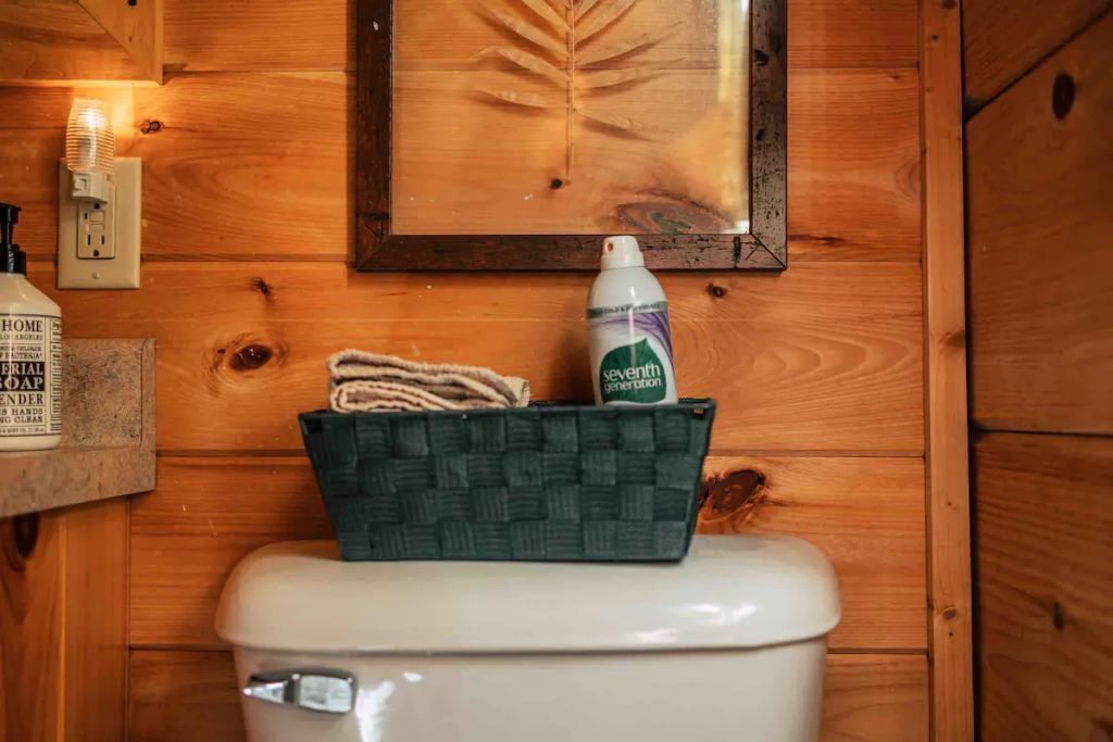 Un baño de madera con inodoro blanco, un cuadro de una hoja enmarco, una botella de jabón Seventh Generation y una cesta tejida con una toalla.