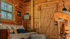Interior acollidor d'una cabana amb elements de fusta, un sofà amb coixins, una làmpada i una porta gran.