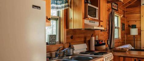 A wooden cabin kitchen with a refrigerator, stove, sink, and microwave.
