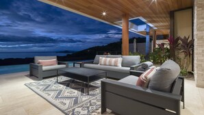 A modern outdoor seating area with a pool, a patterned rug, and a view of the ocean at dusk.