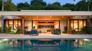 A modern house with a pool, outdoor seating, and a well-lit interior.