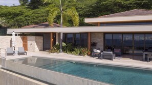 Une maison moderne dotée d’une piscine, d’un espace salon extérieur et offrant une vue sur la verdure environnante.