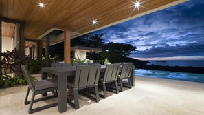 Un espace extérieur aménagé pour prendre les repas, avec vue sur l’océan au crépuscule.
