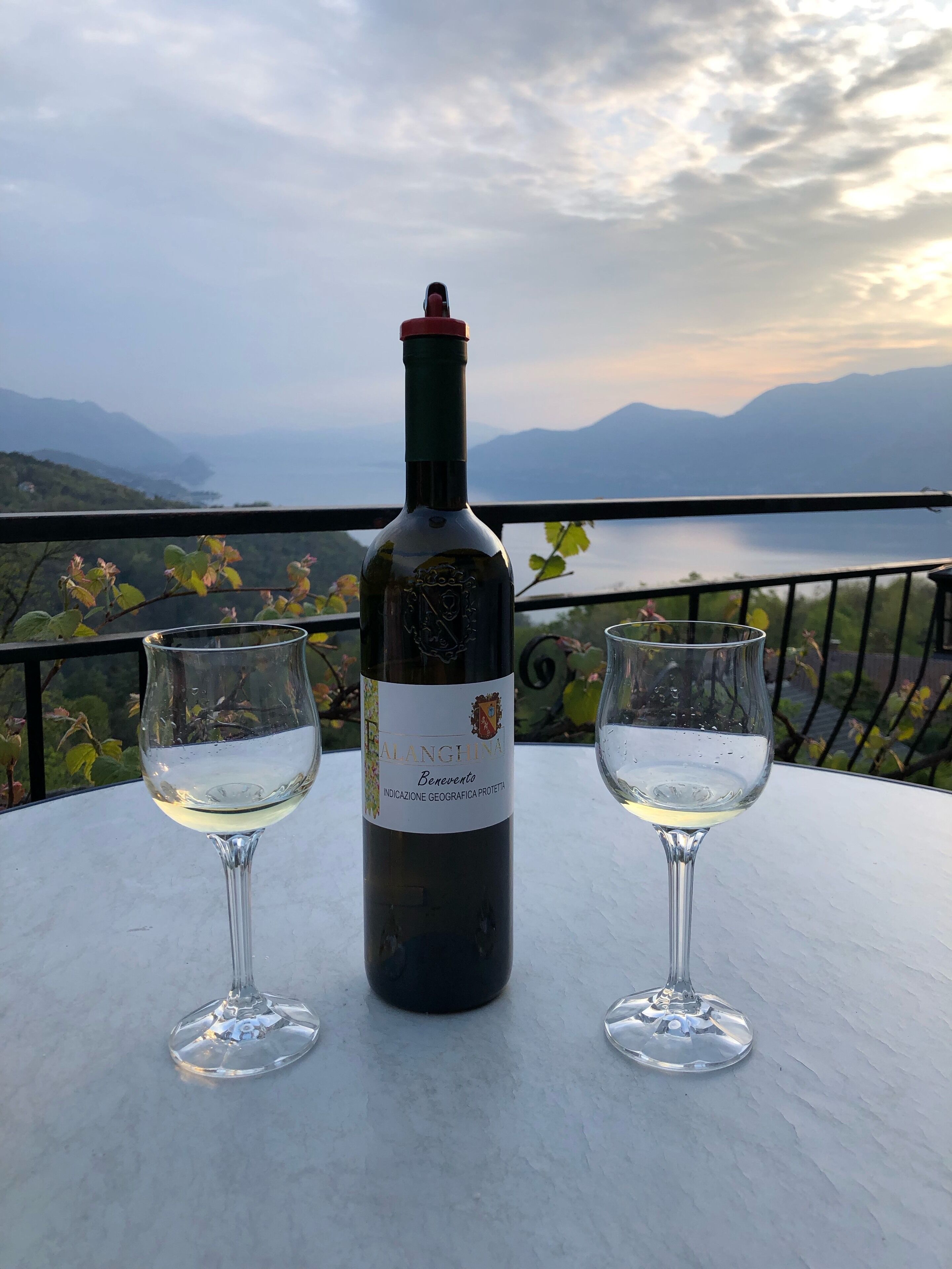 Una bottiglia di vino e due bicchieri su un tavolo con vista panoramica su montagne e un lago.