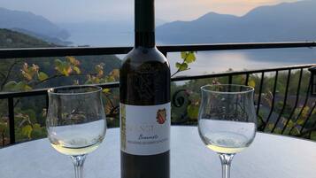 Una bottiglia di vino e due bicchieri su un tavolo con vista panoramica su montagne e un lago.