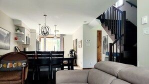 A modern living room with a sofa, dining table, chairs, and a staircase.