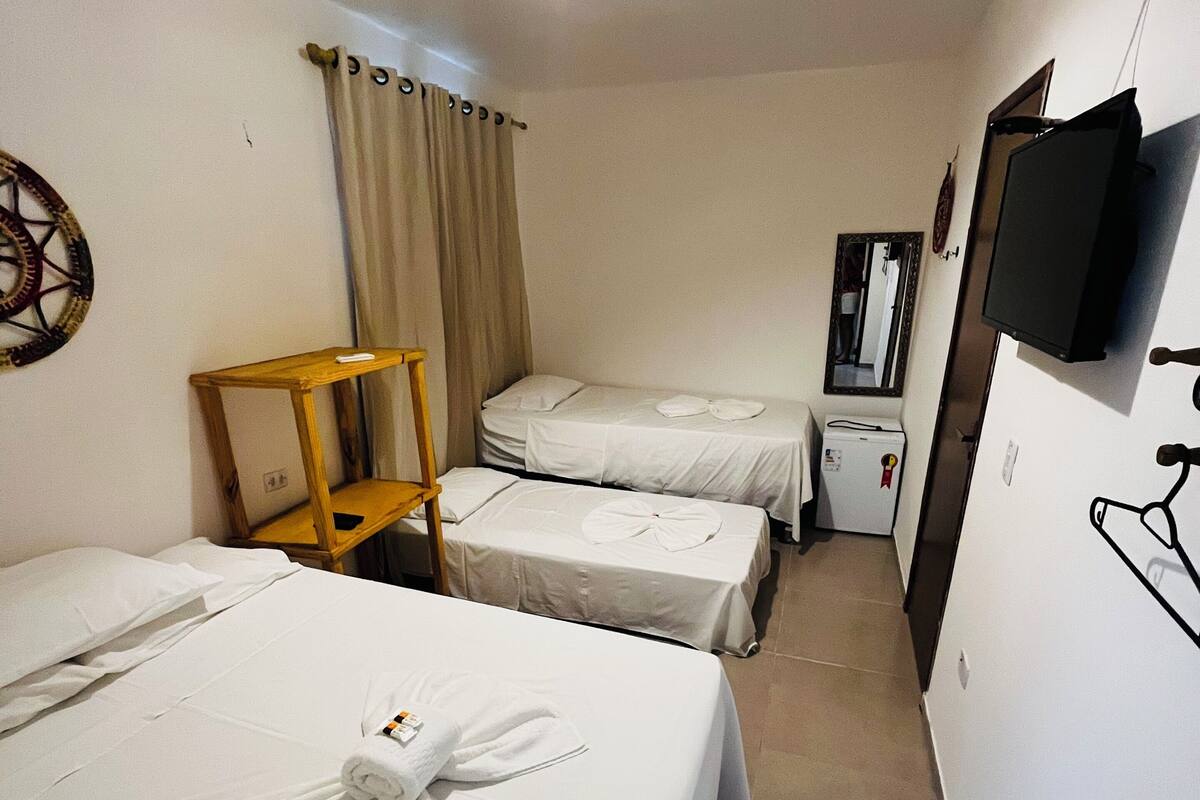 Quarto de hotel com duas camas, uma cadeira de madeira, televisão, espelho e luminária no teto.