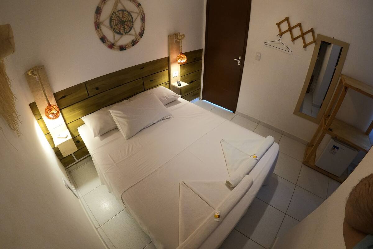 Cama bem arrumada com lençóis brancos, cabeceira de madeira e decoração com bússola fixada na parede.