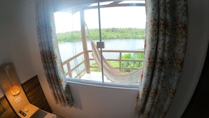 Habitación con ventana que da a una masa de agua, una hamaca y una mesita de noche con lámpara y control remoto.