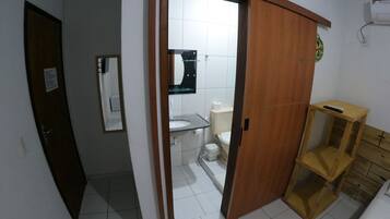 A bathroom with a toilet, sink, and mirror. There is a wooden door leading to another room. A small wooden stool is visible next to the sink.