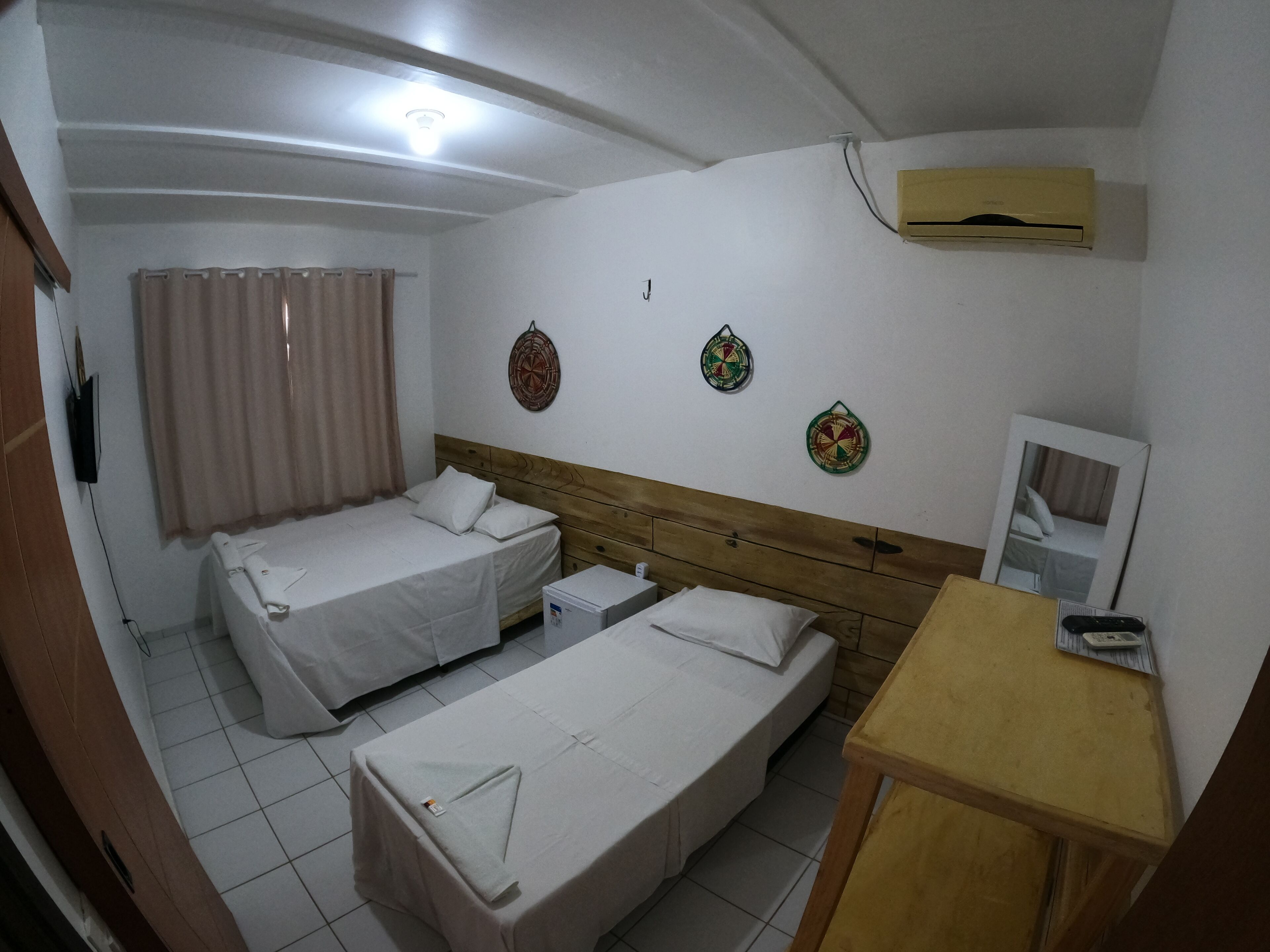 Habitación de hotel con dos camas individuales, cabecero de madera, una mesita, un espejo y adornos en la pared.