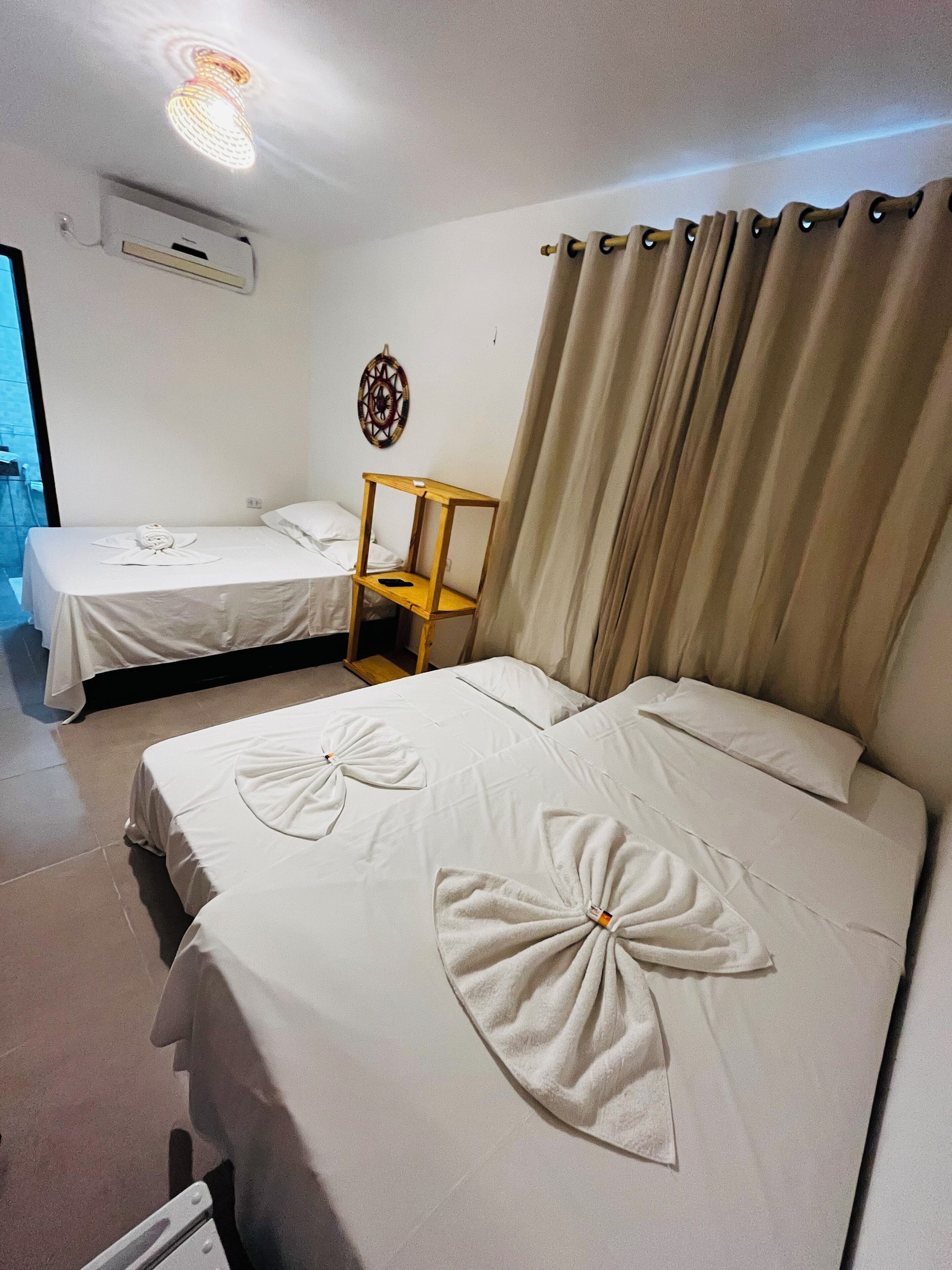 Habitación de hotel con dos camas, una mesita de noche de madera, un aire acondicionado instalado en la pared y una cortina.
