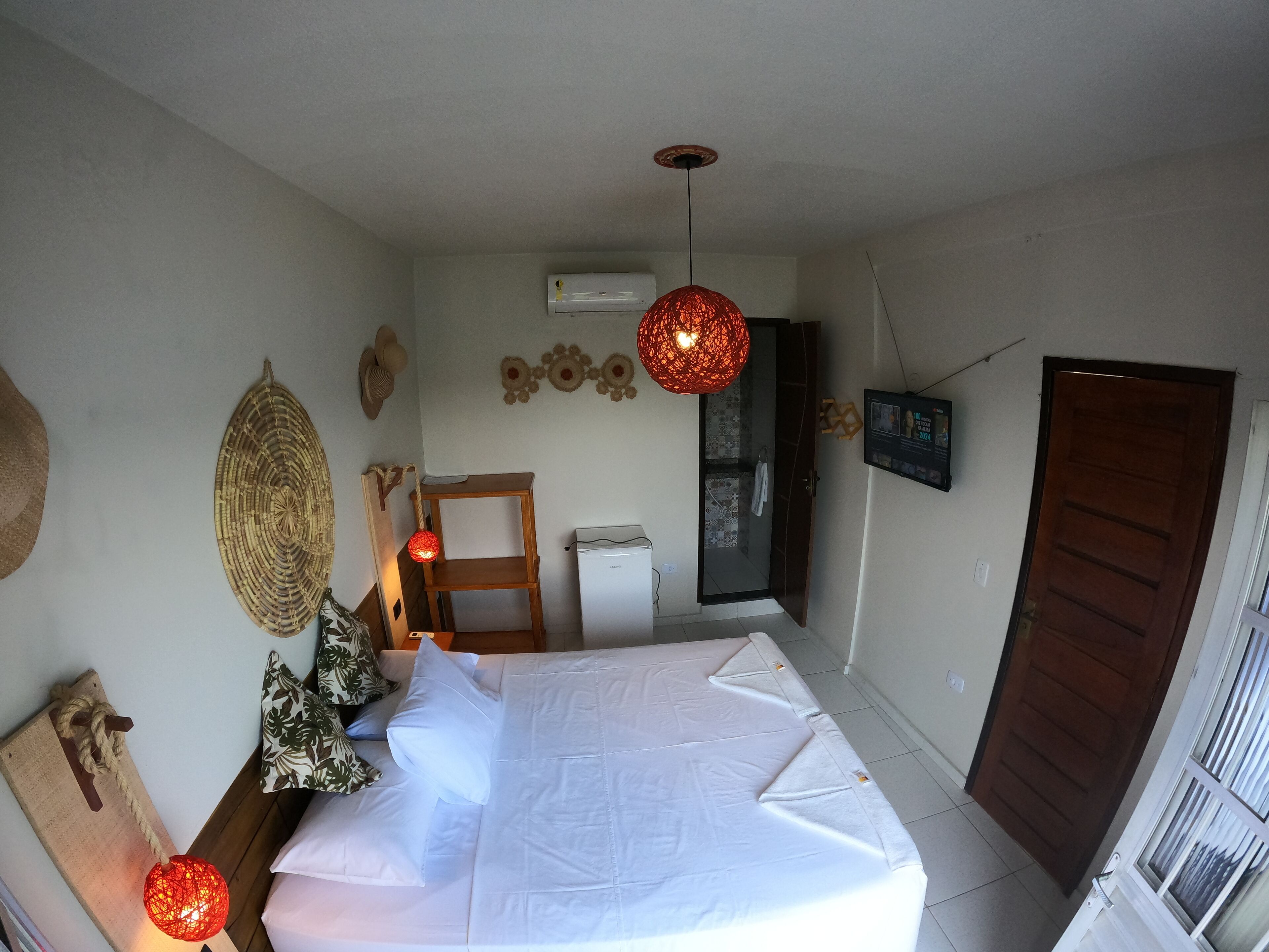 A bedroom with a bed, a wooden headboard, a wall-mounted air conditioner, a door, and a window with curtains.