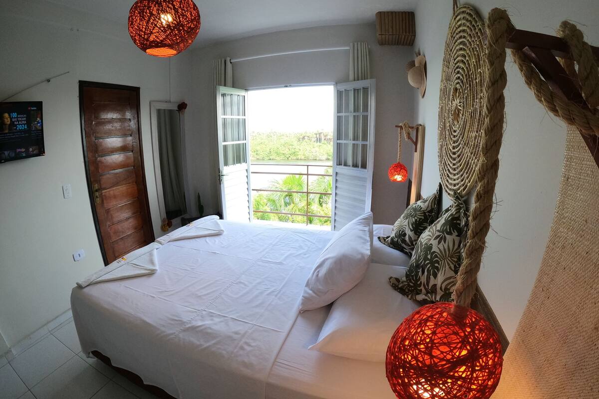 Quarto com cama, janela com cortinas, luminária pendente e porta.