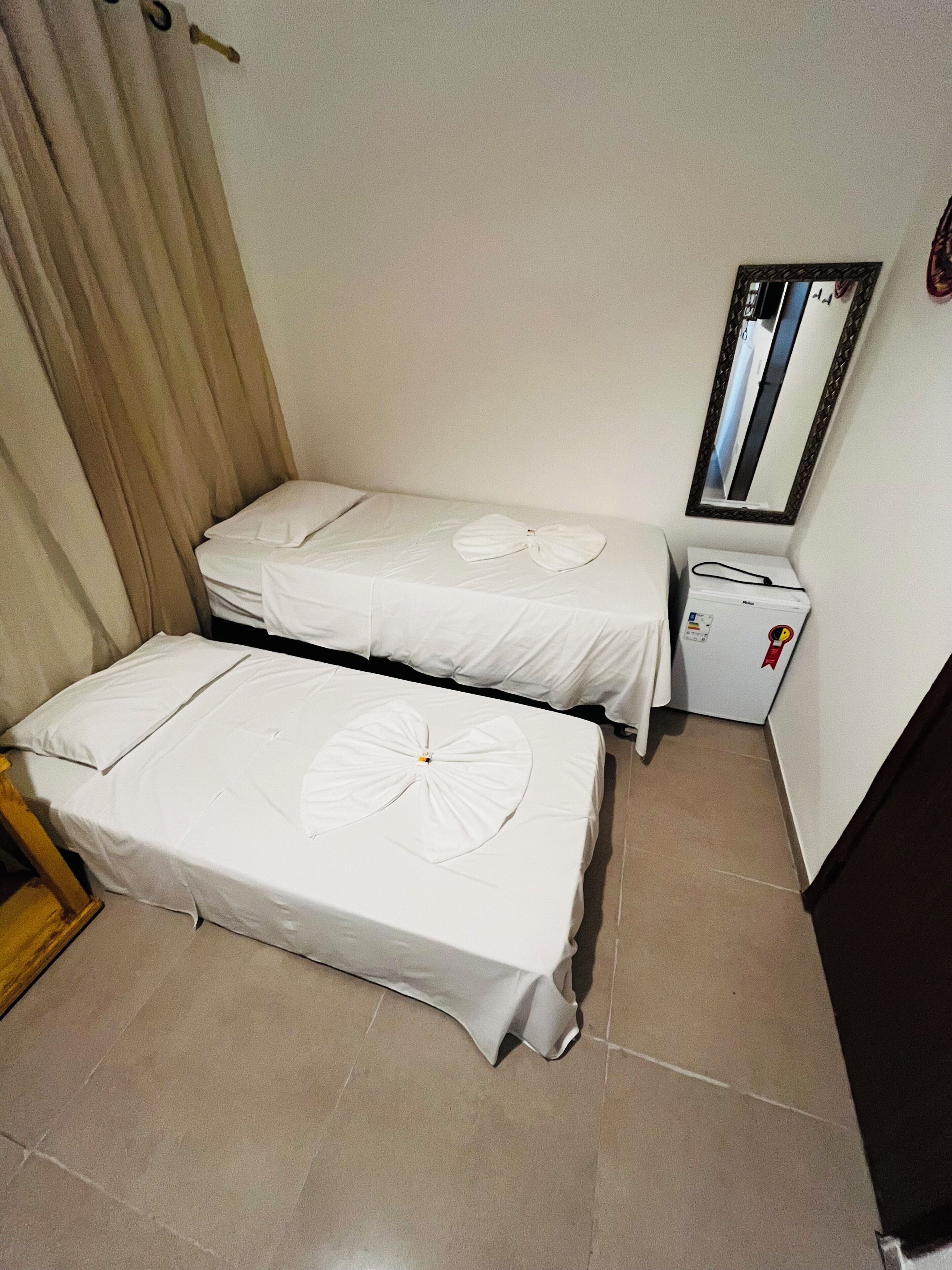 A small hotel room with two single beds, a small table, a mirror, and a heater.