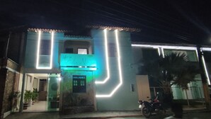 Un edificio con un letrero de neón, una motocicleta estacionada afuera y una palmera cerca.