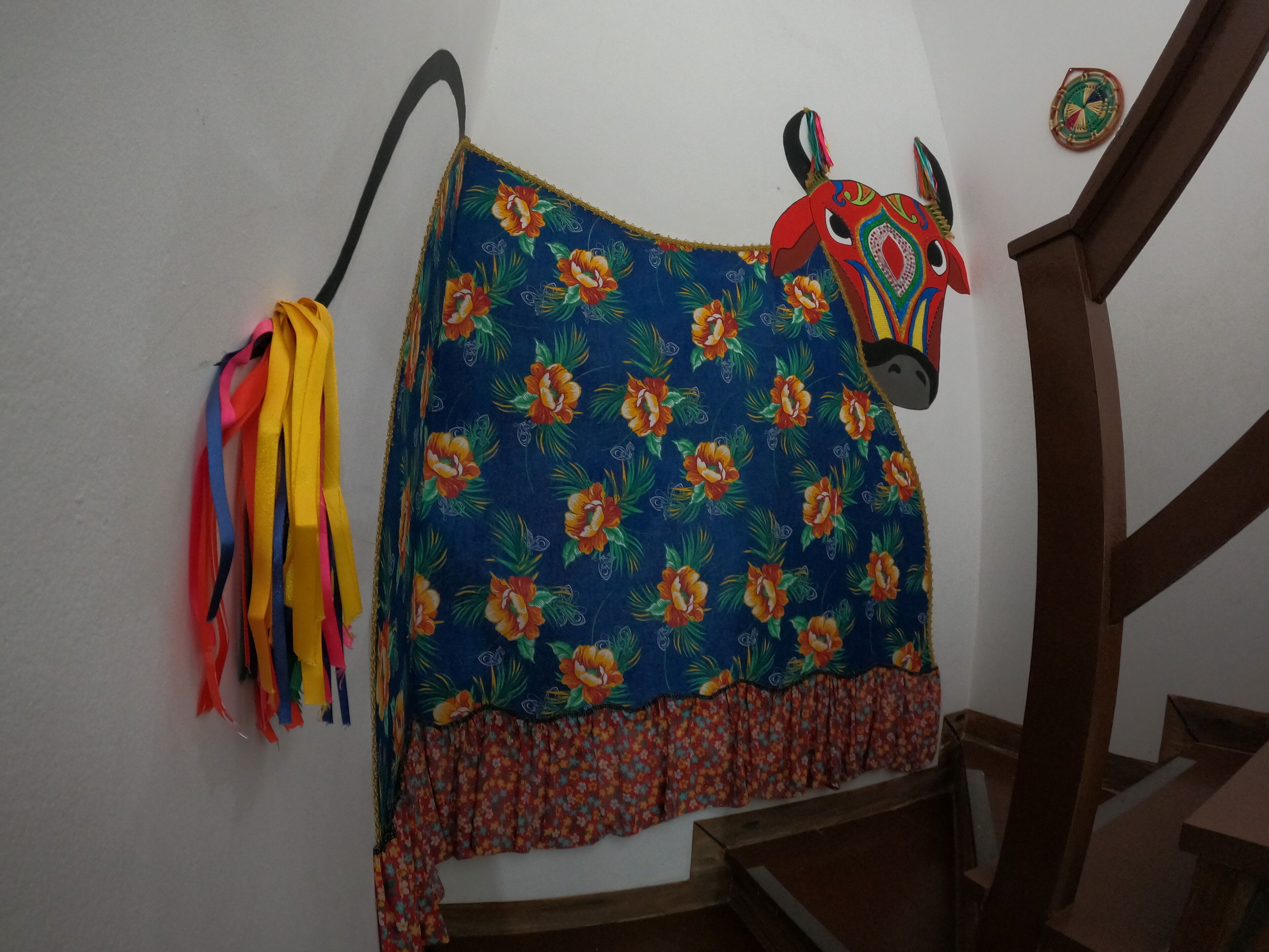 A room with a blue floral-patterned bedspread, a colorful headpiece, and a wooden staircase.