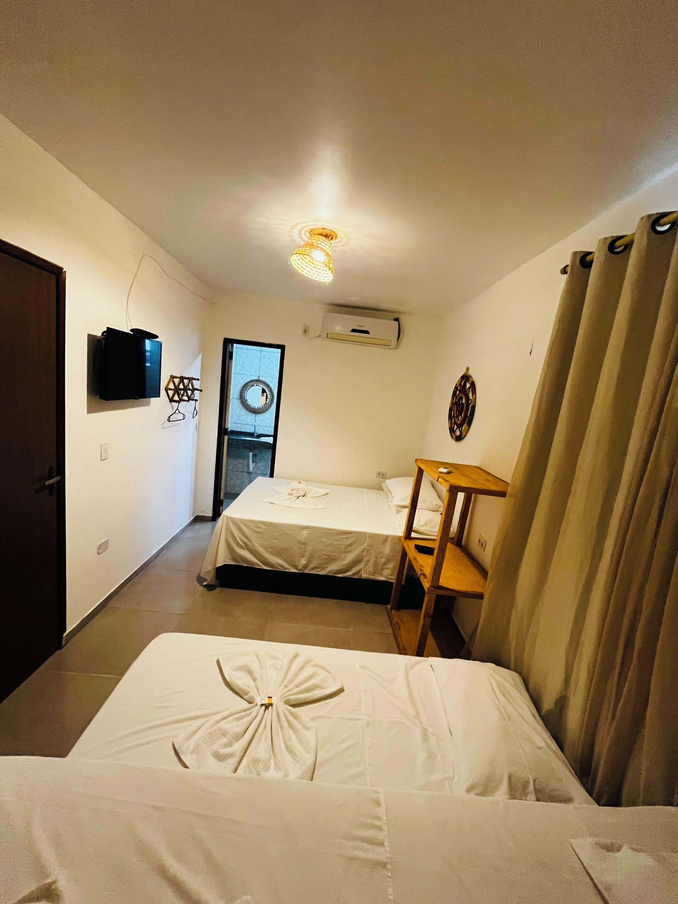 A room with two beds, a small table, a TV mounted on the wall, and an air conditioning unit.