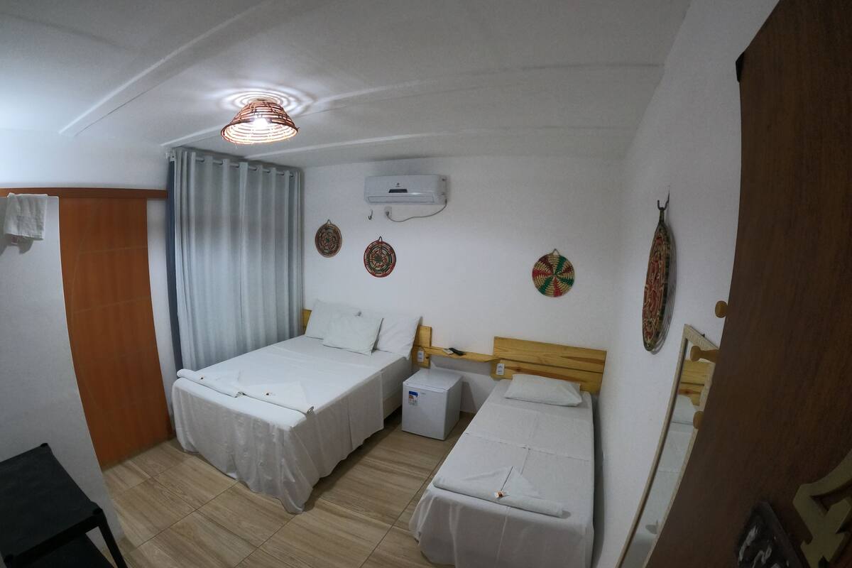 Quarto com duas camas, uma mesa pequena, uma cadeira, unidade de ar condicionado e uma luminária no teto.