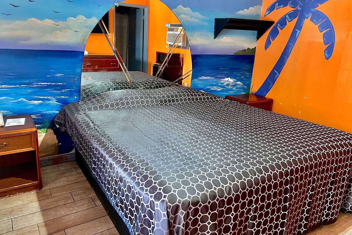 Une chambre avec un lit, une table de chevet en bois et une fresque murale représentant l’océan.
