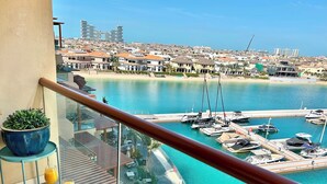 Un balcone con un tavolo apparecchiato per la colazione, vista su una marina con barche e sullo skyline costiero.