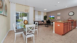 A modern kitchen with a dining area, featuring a glass table, white chairs, and a kitchen island with a sink and cabinets.