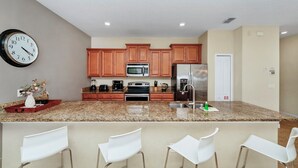 A modern kitchen with granite countertops, stainless steel appliances, wooden cabinets, and a clock on the wall.