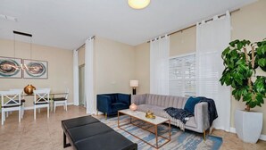 A modern living room with a sofa, coffee table, and a dining area with chairs and a table.