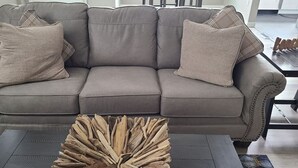 Un canapé gris agrémenté de deux coussins décoratifs à motifs et une table basse en bois originale placée devant.