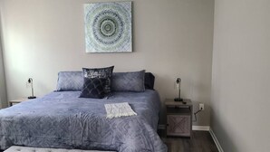 Une chambre à coucher avec un grand lit, deux tables de chevet, un banc et une œuvre d’art accrochée au mur.