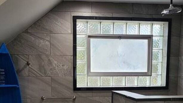 Une salle de bain avec un plafond en pente, une fenêtre à vitre dépolie et une étagère bleue.