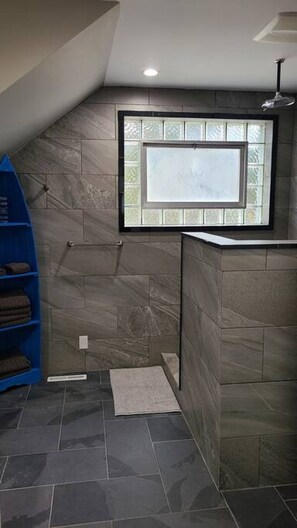 A bathroom with a sloped ceiling, a window with frosted glass, and a blue shelving unit. - Lovely 1 bedroom rental. Newly renovated! (Port Washington)