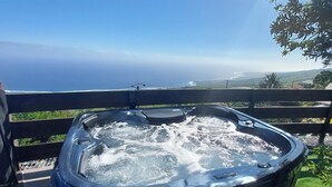 A hot tub on a deck with a view of the ocean and hills.