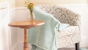 A corner room with a patterned sofa, a small wooden table with a vase, and a framed picture on the wall.