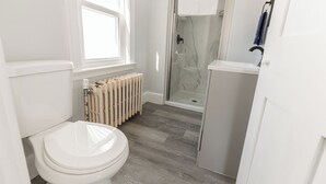 A bathroom with a toilet, a shower with a glass door, and a radiator.