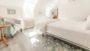 A bedroom with a bed, a chair, a table, and a radiator.
