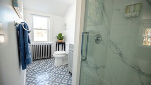 A bathroom with a patterned floor, a toilet, a radiator, and a glass shower enclosure.
