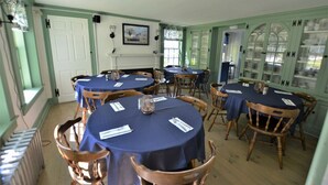 A dining area with round tables covered in blue tablecloths, wooden chairs, and a white door with a green frame. - Room 08 - King Room  - Handicap accessible (Francestown)