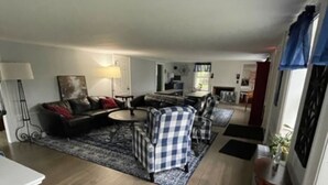A spacious living room with a sofa, armchairs, and a rug. A small dog is visible in the foreground. - Room 08 - King Room  - Handicap accessible (Francestown)